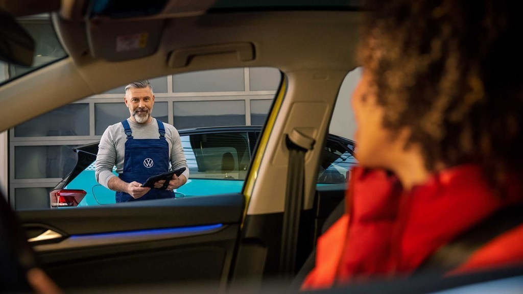 Meccanico sorridente parla con una cliente seduta in macchina
